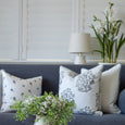 Coastal Pearl Table Lamp with white shade and textured ceramic base styled behind a blue sofa with floral cushions, white orchids and a rattan tray in a Hamptons living room.