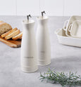 Cream speckled stoneware oil and vinegar bottles styled on a kitchen benchtop with fresh bread and rosemary