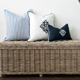 Diamond Monogram White Cushion Cover styled with navy and ticking stripe cushions on a woven rattan storage bench.