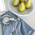 Ellis blue striped tea towel styled on a kitchen bench with measuring cups, pears and marble serving bowl in a coastal kitchen.