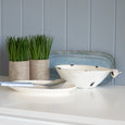 Coastal styled white whale dish displayed on a console beside decorative greenery and layered coastal home décor.