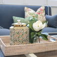 Floral porcelain canister with gold lid styled on a rattan tray alongside decorative accessories and white magnolia stems in a Hamptons-style living room.