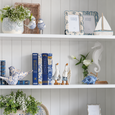 Hamptons Book Box Set of 4 displayed on white shelving with blue and white ceramics, coastal bird ornaments, decorative photo frames and greenery.