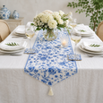 Blue and white floral table runner styled on a coastal dining table with white flowers, wine glasses and layered white dinnerware