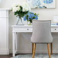 Artificial white hydrangea arrangement styled on a white desk with coastal decor and soft blue artwork in a bright elegant interior.