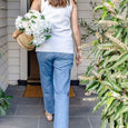 Woman carrying white faux hydrangea stems in a woven basket at a coastal style home entrance.