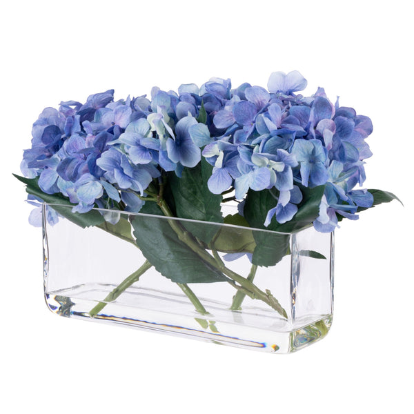Blue faux hydrangea arrangement styled in a clear rectangular glass trough vase.