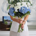 Woman holding a large blue and white hydrangea bouquet in a bright Hamptons-inspired interior with coastal decor.