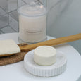 White marble soap dish styled in a soft coastal bathroom with candle, soap bar and natural timber bath brush