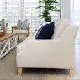 Side profile of Knightsbridge natural linen sofa with white piping and timber legs in a coastal living room.
