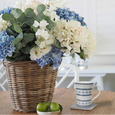 Le Petite blue and white ceramic mug styled on a marble coaster beside a wicker basket of blue and white hydrangeas on a coastal timber dining table.