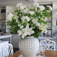 Large faux white lilac arrangement styled in a white ceramic vase on a Hamptons-style dining table.