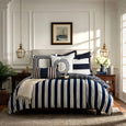 Navy and white striped linen cushions styled on a classic Hamptons-inspired bed with coastal decor and layered blue accents.
