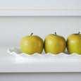 White scalloped porcelain serving platter styled with green apples on a coastal-inspired shelf.