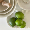 White porcelain scalloped serving platter styled with fresh limes and neutral kitchen decor.