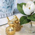White magnolia floral arrangement in glass vase styled with gold bird sculptures on a white scalloped tray.