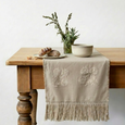 Neutral embroidered table runner styled on wooden table with ceramics and greenery