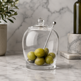 Glass olive jar filled with green olives and stainless steel serving spoon, perfect for grazing tables and entertaining