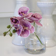 Realistic purple orchid arrangement in a glass vase styled with white candle holders in a Hamptons-inspired interior