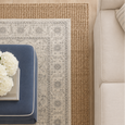 Overhead view of the Parker White Rug layered over the Payton Natural Rug with a navy upholstered ottoman, white hydrangeas, and a neutral sofa in a relaxed coastal living room setting.