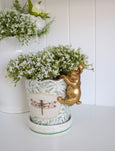Gold pot sitter rabbit figurine hanging over the rim of a white ceramic planter.