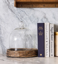 glass dome with woven base styled on marble bench beside cookbooks