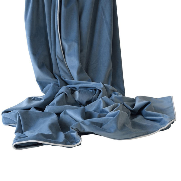 Ocean blue velvet throw with white piping draped softly, showcasing smooth texture and luxurious finish