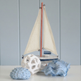 Sailboat Docks Small decorative sailboat styled with coastal coral and shell accents on a white shelf, creating a relaxed Hamptons-inspired coastal display.