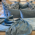 San Diego Ocean Cushion layered with tonal blue velvet cushions and coordinating ocean blue bedding in a styled bedroom.