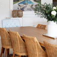 Large woven seagrass lantern styled on a white sideboard beside a timber dining table in a relaxed coastal dining room.