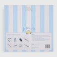 A set of La Dolce Vita Seaside Crackers in bright coastal prints, tied with yellow bows, displayed in a striped gift box. Includes seaside-themed gifts, mottos, and paper crowns.
