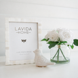 Sorrento Scallop Bone Photo Frame styled on a white shelf beside white faux roses in a glass vase and a ceramic bird ornament for relaxed coastal styling.