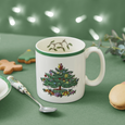 Spode Christmas Tree mug styled on a festive green tabletop with holiday treats, lights and seasonal tableware.
