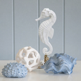 White seahorse coastal sculpture styled with decorative blue shell, white coral orb and coastal accessories on a white console table, creating an elegant Hamptons-inspired coastal vignette.