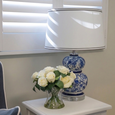 White Shade with Black Trim styled on a blue and white ceramic table lamp beside white roses in a Hamptons-inspired bedroom setting.