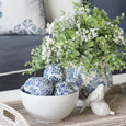 Willow Blue & White Ceramic Decor Balls styled in a white bowl on a rattan tray with blue and white vase and greenery.