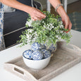 Paume Whitewash Rattan Tray styled on a white coffee table with blue and white ceramics and faux greenery.