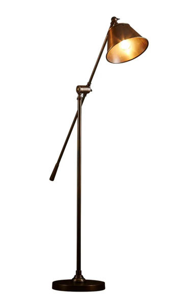 Winston adjustable floor lamp with brass base and angled metal shade beside sofa