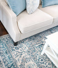 Bridgeport Blue rug styled under a light-coloured sofa, showing textured blue and ivory pattern in a coastal living space