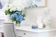 White hydrangea arrangement styled on a desk with coastal home décor and soft neutral furnishings