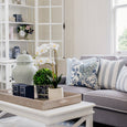 Bright Hamptons-style living room with grey sofa styled with Portsea blue floral and striped cushions, white coffee table and coastal décor